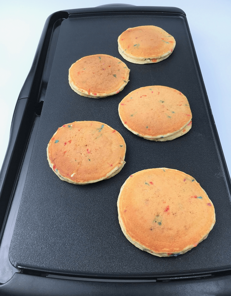 Golden brown funfetti pancakes cooking on an electric griddle