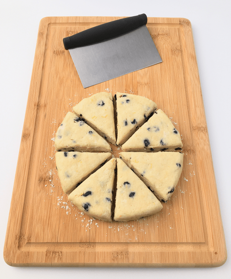 Lemon blueberry scone dough formed into a circle and cut into 8 equal wedges on a cutting board