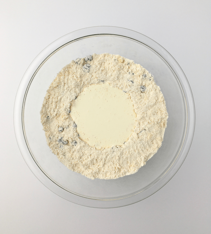 Glass bowl of dry ingredients and blueberries with a well formed in the center filled with heavy cream