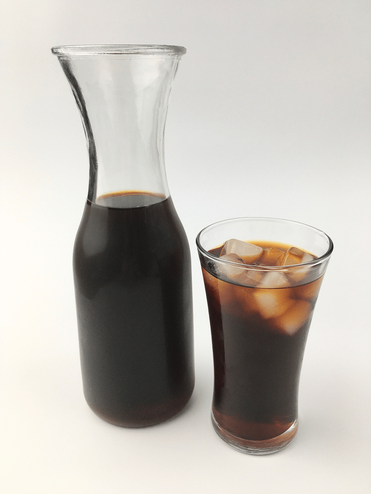 Cold brew iced coffee in a glass with ice next to a full carafe