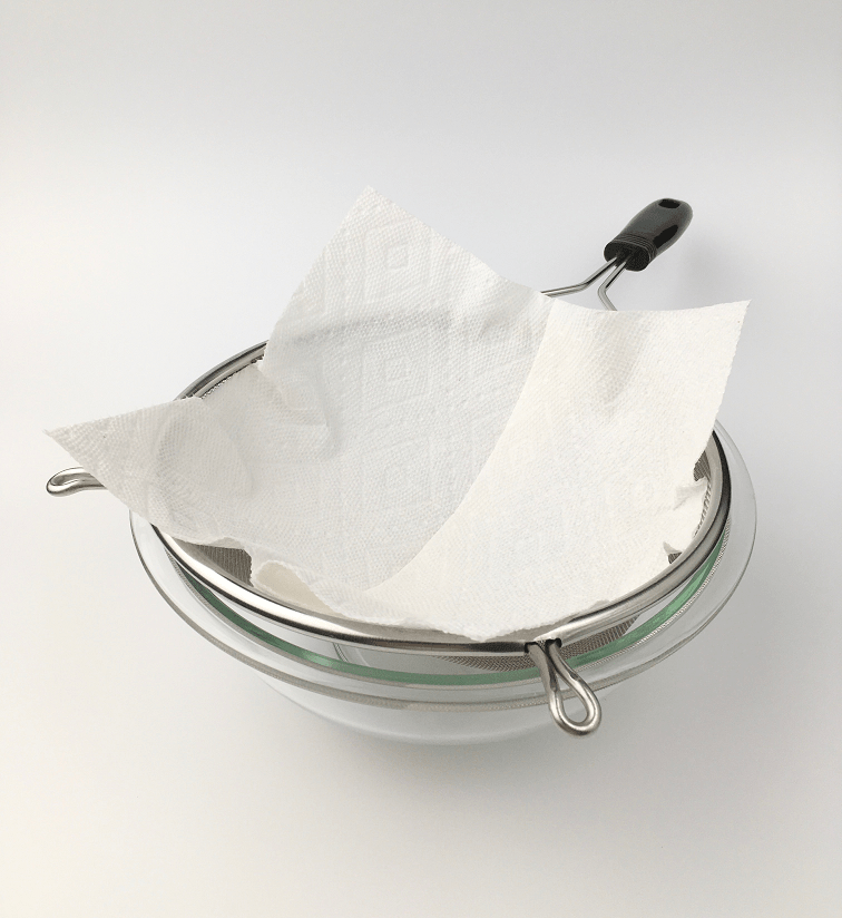 mesh strainer lined with a paper towel over a large glass bowl