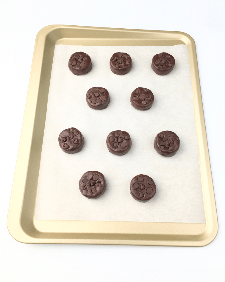 Slightly flattened balls of double chocolate chip cookie dough on a baking sheet with extra chocolate chips placed on top