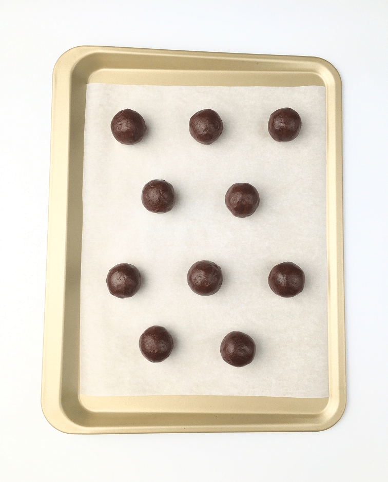 Balls of double chocolate chip cookie dough in rows on a parchment paper lined baking sheet