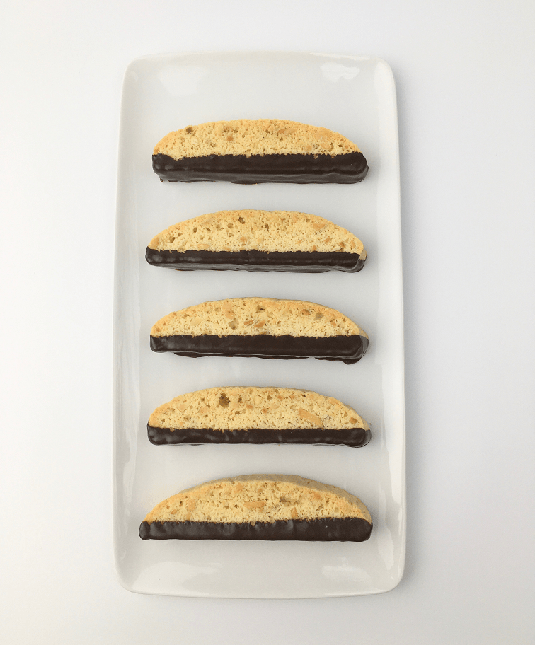 Baked vanilla almond biscotti half covered in chocolate on a white rectangular plate