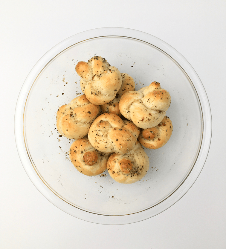 Baked garlic knots in a glass bowl tossed with garlic, oil, and seasonings