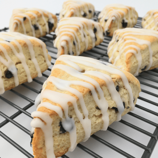 Lemon blueberry scones baked to golden brown on a cooling rack and drizzled with lemon glaze