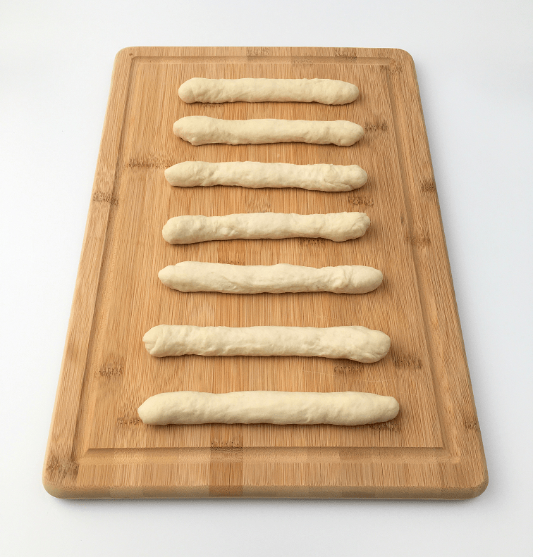 Portions of pizza dough rolled into ropes on a wooden cutting board