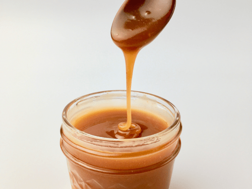 Homemade caramel sauce dripping off a wooden spoon into a glass jar