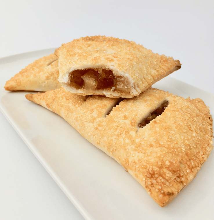 Apple hand pies on a plate with one pie cut in half showing the apple cinnamon filling