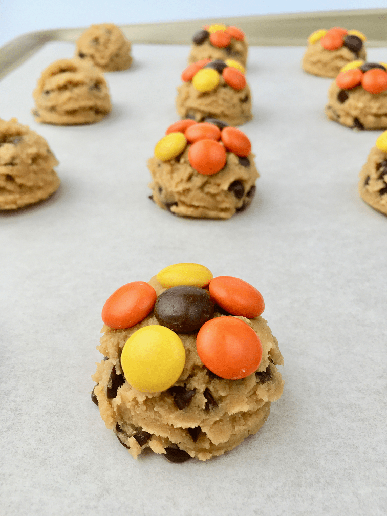 Scooped Reese's Pieces peanut butter cookie dough on a baking sheet topped with Reese's pieces