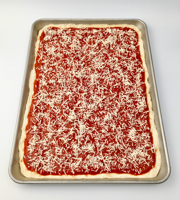 Tomato pie topped with tomato sauce and parmesan cheese before baking