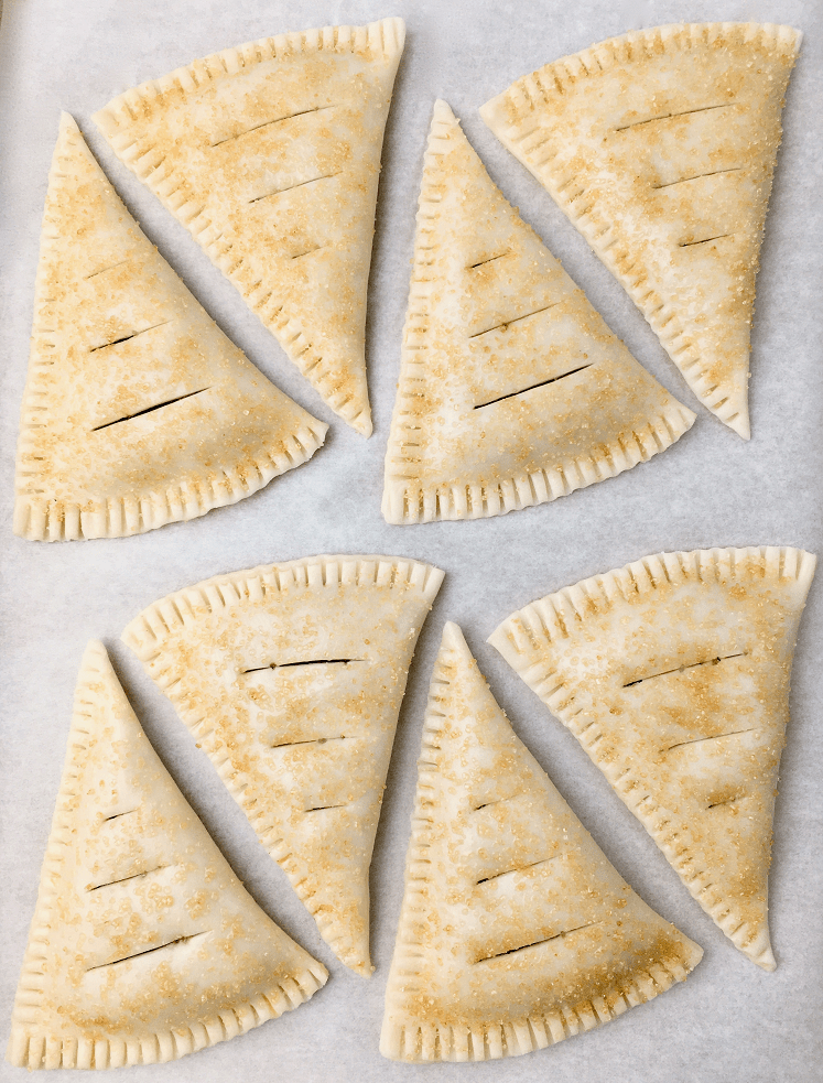 Formed hand pies with egg wash and a sprinkling of raw sugar on a baking sheet