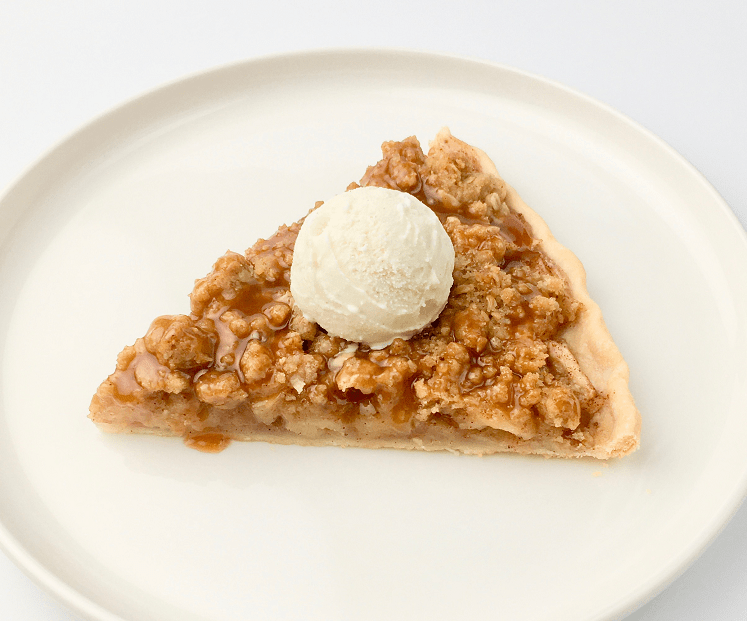 Slice of apple pie pizza with a scoop of vanilla ice cream on a white plate