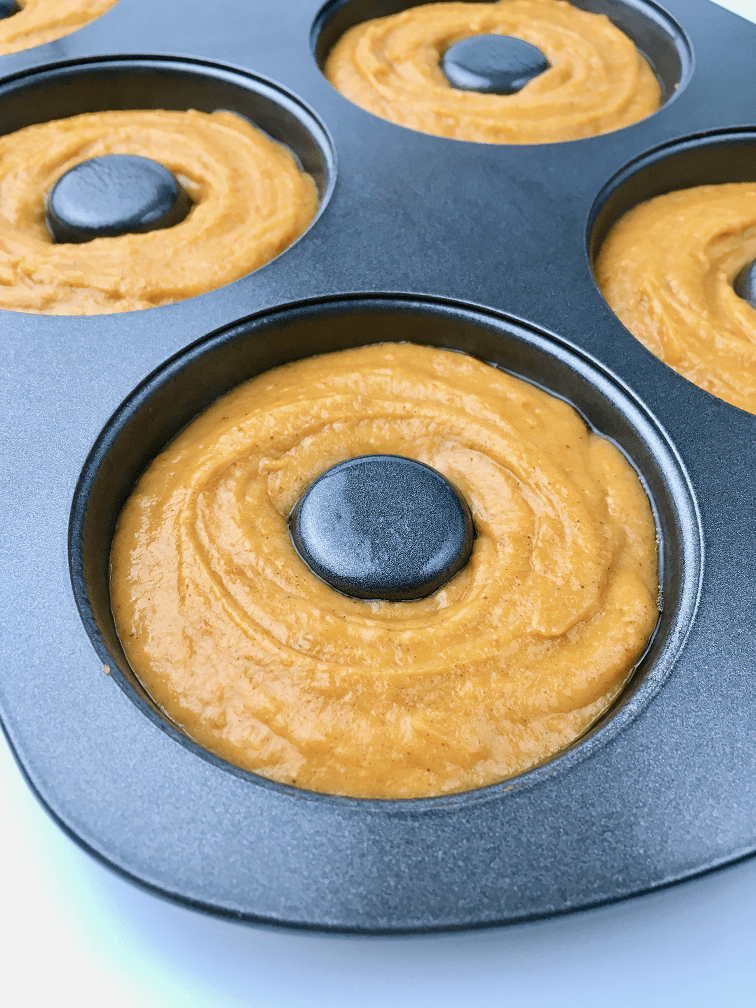 Pumpkin donut batter piped into a donut baking pan.