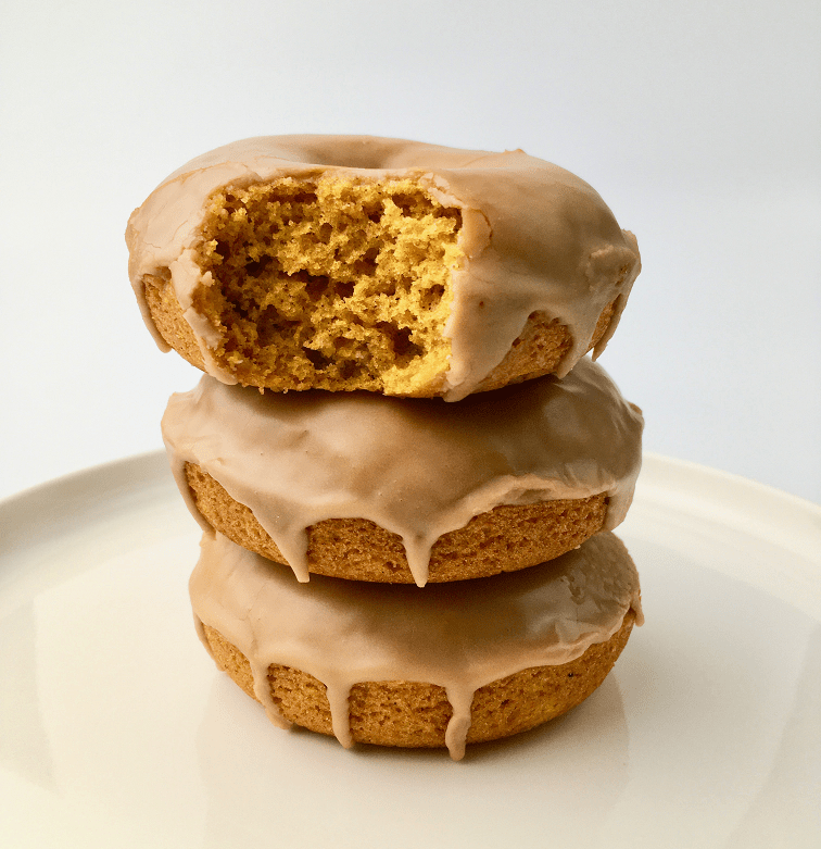 Finished maple pumpkin donuts stacked on a white plate.