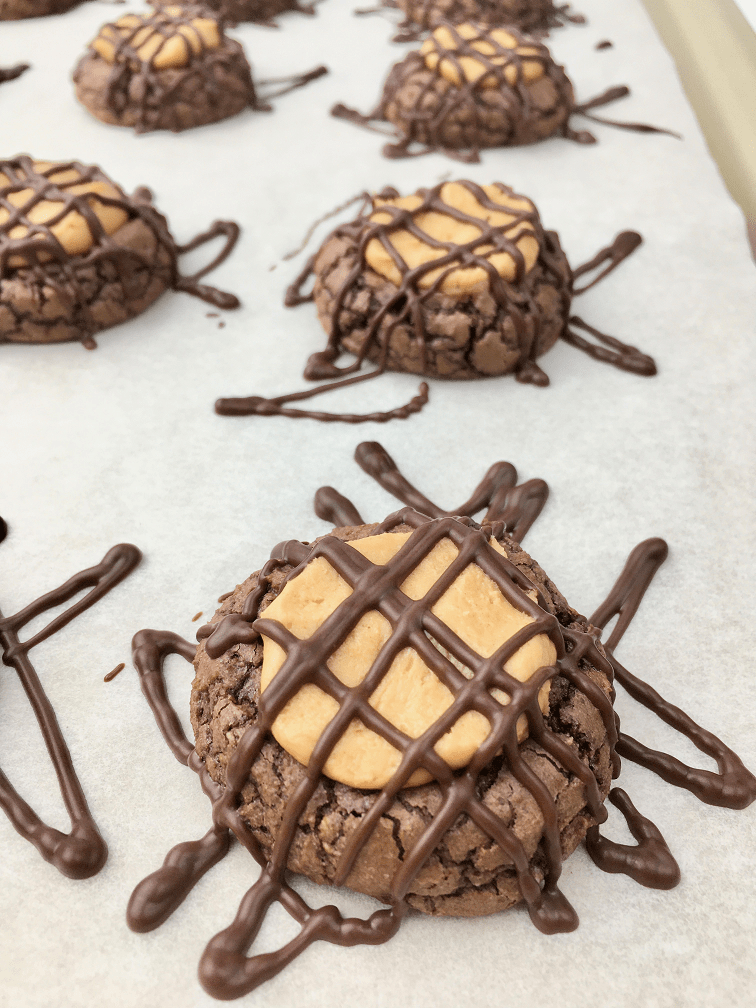 Buckeye cookies on a baking pan topped with peanut butter and drizzled with chocolate