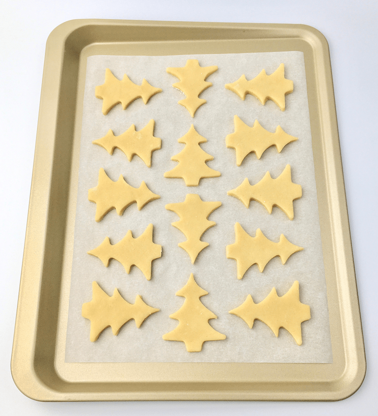 Christmas sugar cookie dough shaped into Christmas trees on a parchment lined baking pan