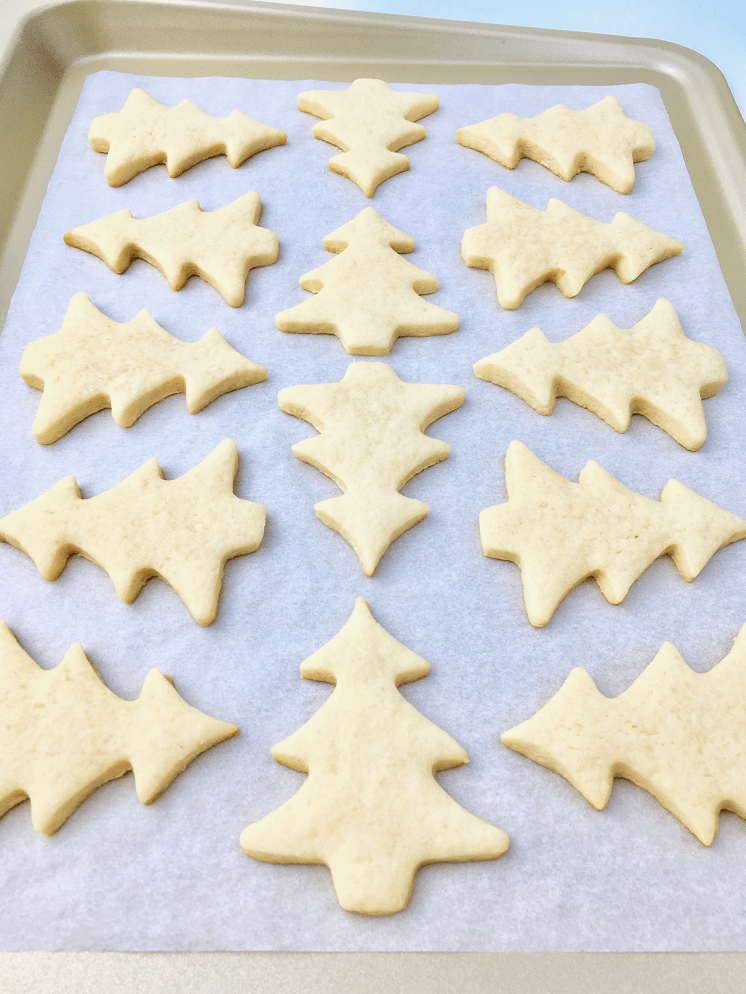 Christmas sugar cookie dough shaped into Christmas trees on a parchment lined baking pan