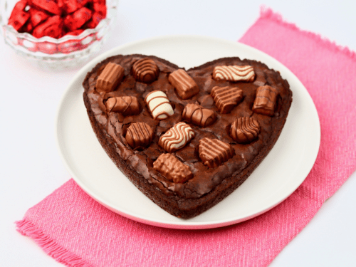 Finished heart shaped box of chocolates brownie next to a glass bowl of Valentine’s chocolate hearts.