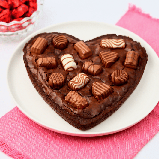 Finished heart shaped box of chocolates brownie next to a glass bowl of Valentine’s chocolate hearts.