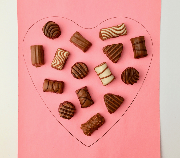 Chocolates arranged into the shape of a heart on a piece of pink paper.