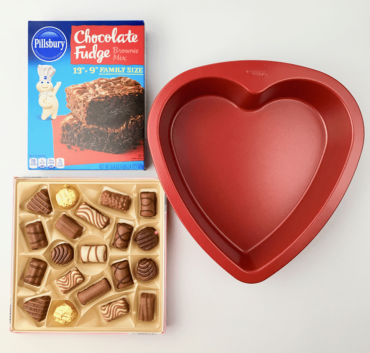 Box of brownie mix, red heart cake pan, and box of chocolates arranged on a table.