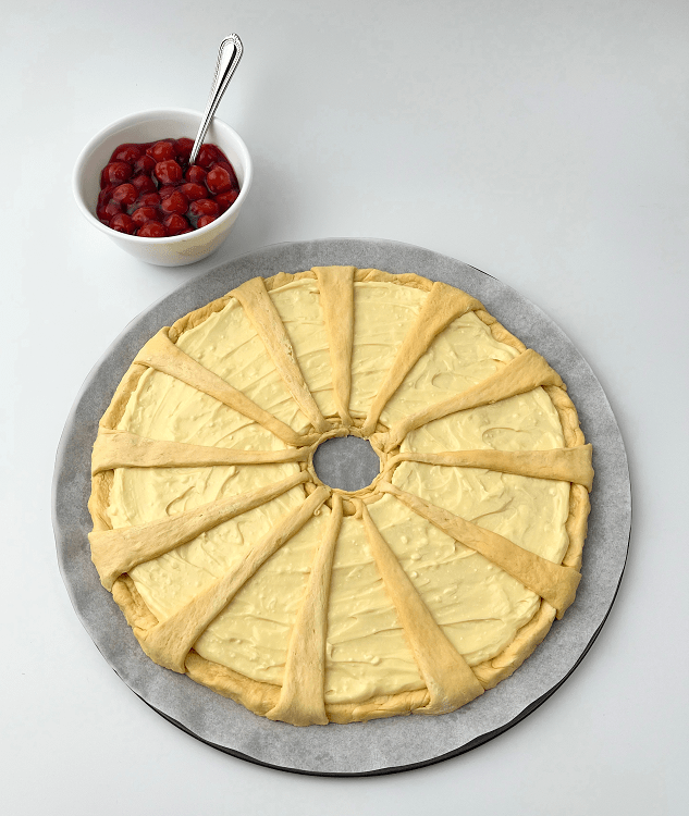 Crescent ring spread with cream cheese next to a bowl of cherry pie filling for topping