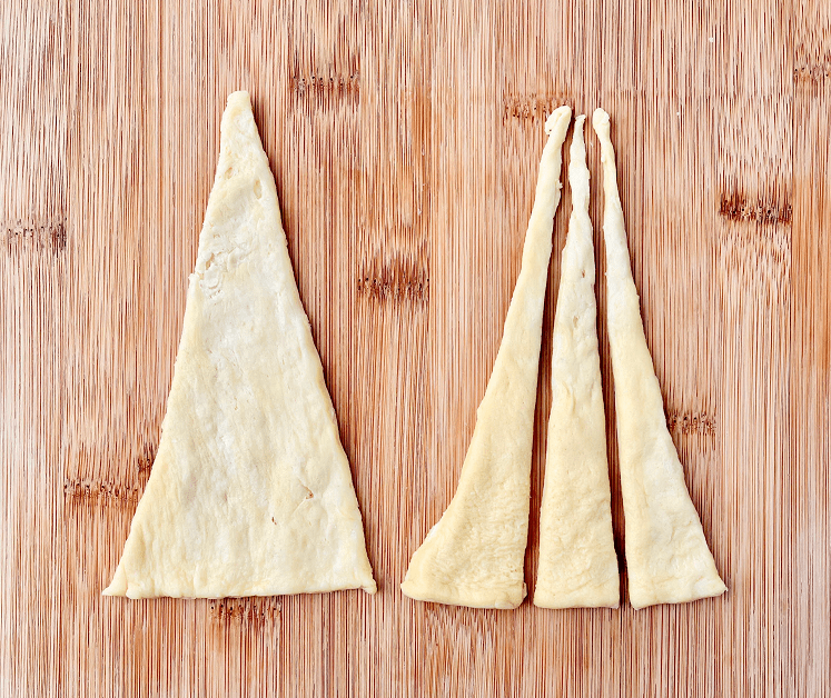 Triangle of crescent dough cut into 1/3’s on a wooden cutting board.