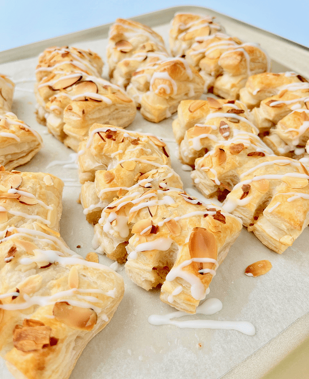 Baked bear claws drizzled with icing on a baking pan