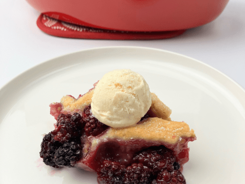 Blackberry cobbler on a white plate topped with vanilla ice cream