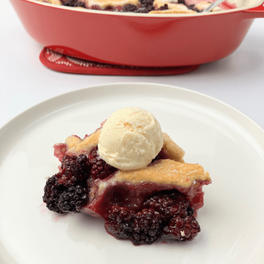 Blackberry cobbler on a white plate topped with vanilla ice cream