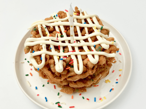 Stacked funfetti funnel cakes with frosting and sprinkles on a plate