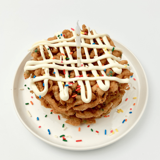 Stacked funfetti funnel cakes with frosting and sprinkles on a plate