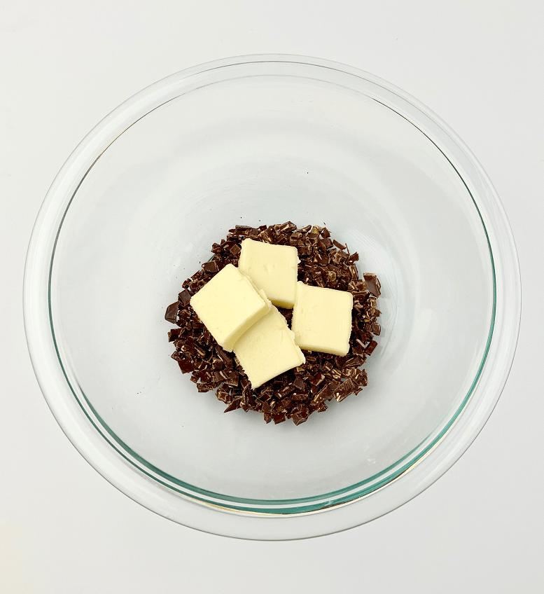 Chopped chocolate and sliced butter in a glass bowl.