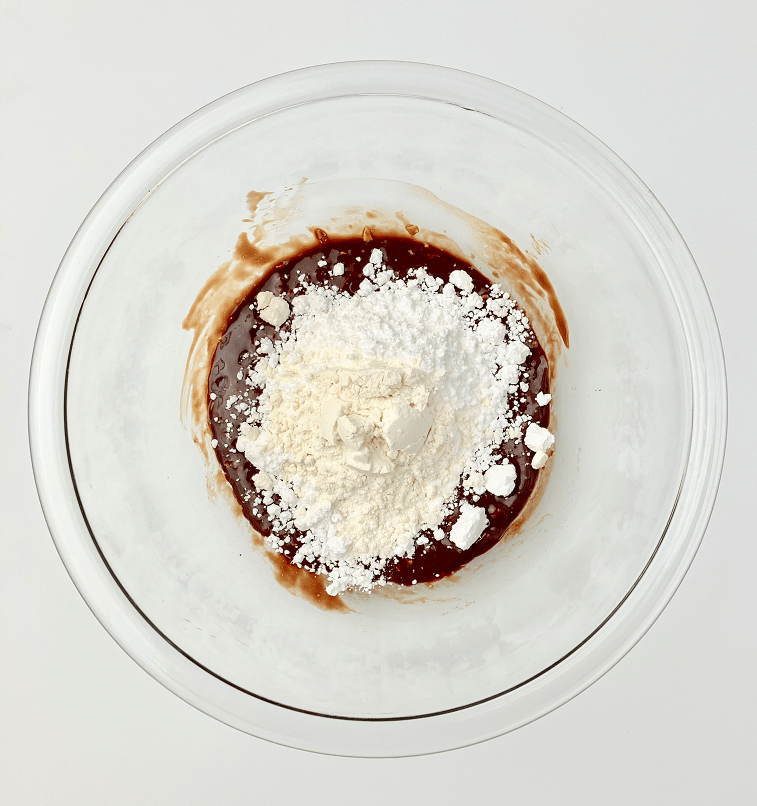 Chocolate orange lava cake batter in a glass bowl with powdered sugar and flour.