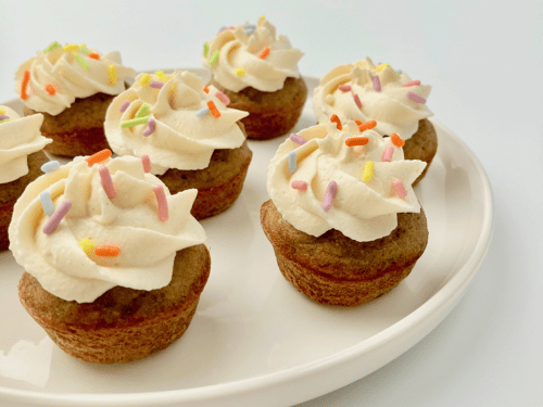 Peanut butter banana mini pupcakes with frosting and sprinkles on a plate.