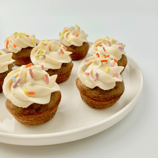 Peanut butter banana mini pupcakes with frosting and sprinkles on a plate.