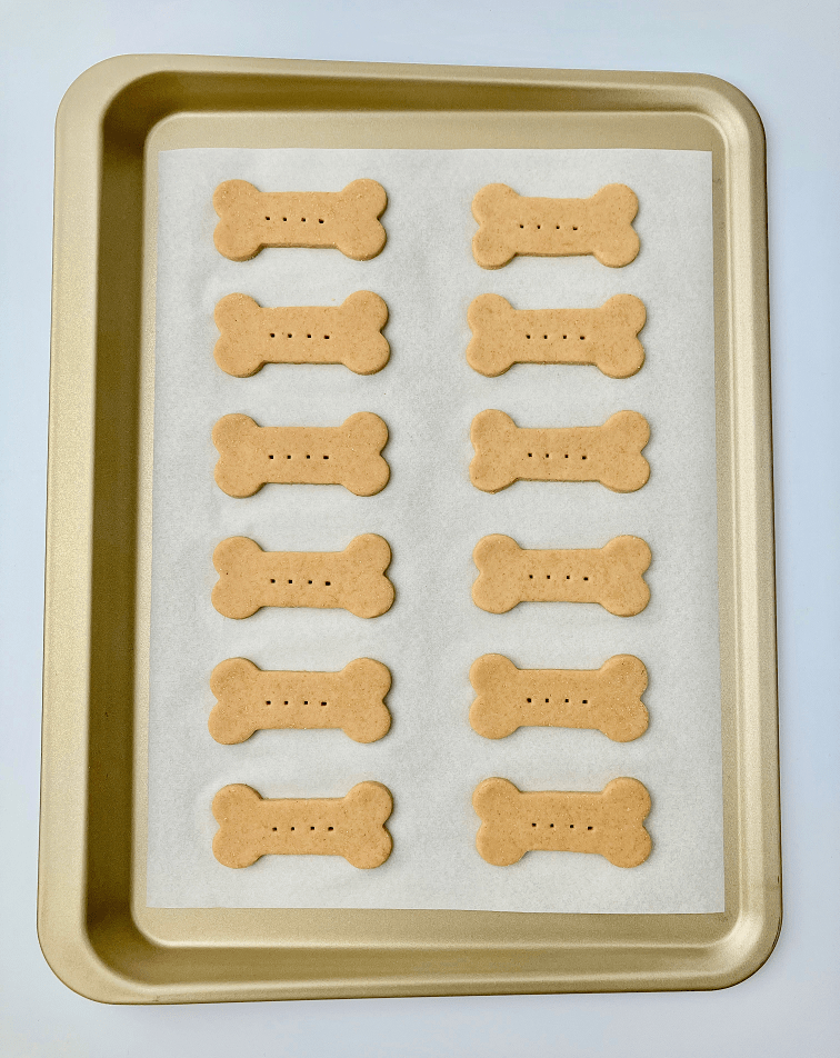 Chicken dog treat dough shaped into bones on a baking pan.