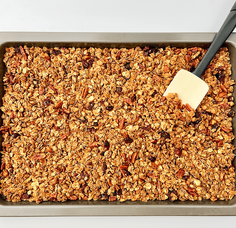 Gingerbread granola on a baking pan with spatula.