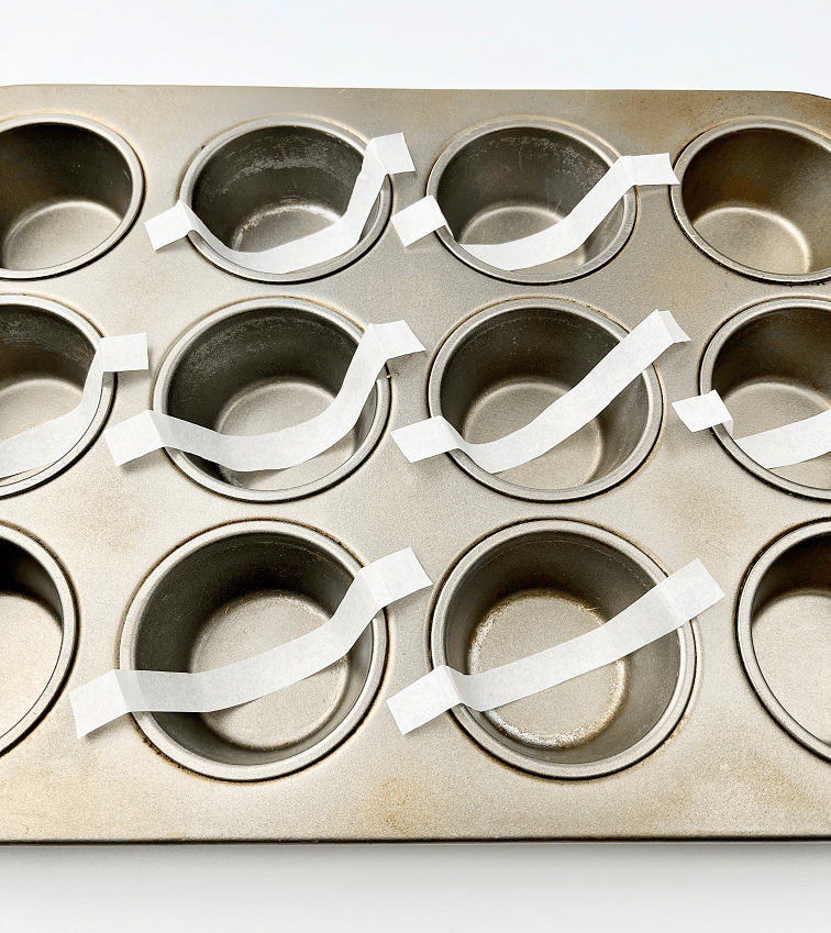 Muffin pan lined with parchment paper strips.