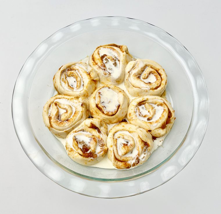 Unbaked pumpkin pie cinnamon rolls in glass pie plate.