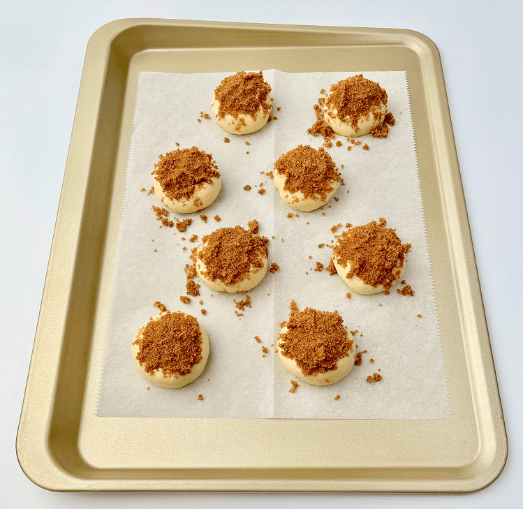 Unbaked bagel bites with cinnamon crunch topping on a baking pan.