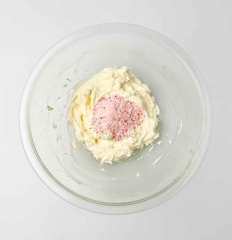 Peppermint frosting in a glass bowl topped with crushed candy canes.